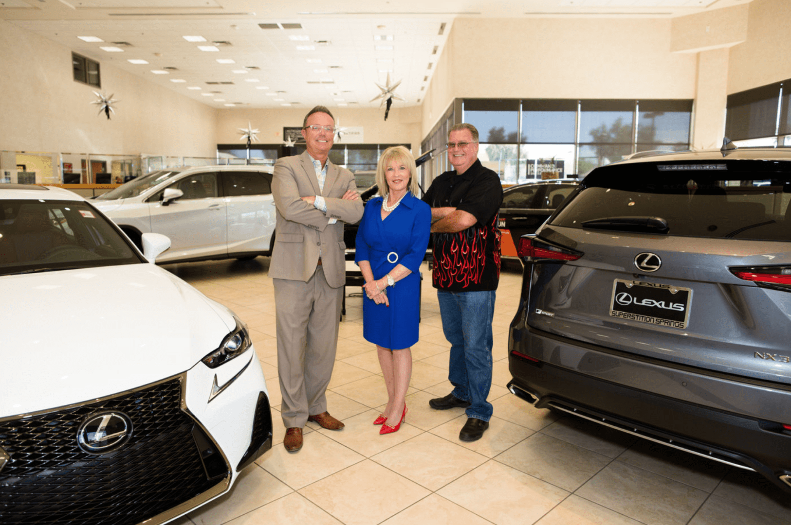 Three adults smiling in a car dealership, standing between a white and a gray lexus car.