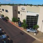 Aerial view of an infiniti dealership building with parked cars and green landscaping under a clear sky.