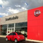 A red fiat car parked in front of the fiat dealership in scottsdale with a bright sky and clouds overhead.