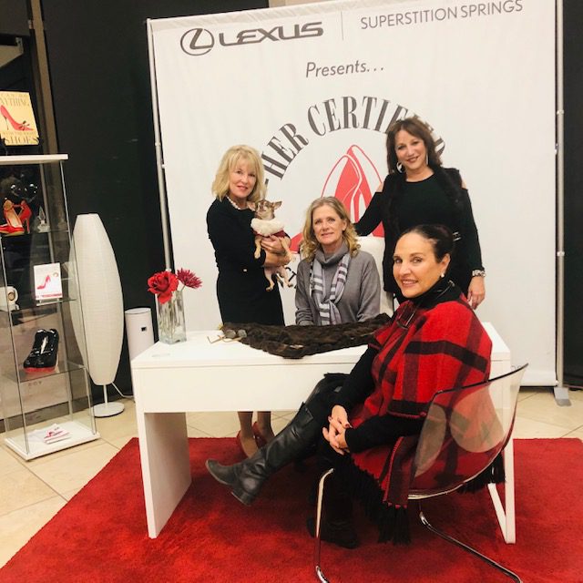 Four women posing at a promotional event booth with a lexus and superstition springs logo, one holding a cat.