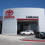 A toyota dealership building with the camelback logo, featuring glass windows and parked cars in front under a clear blue sky.