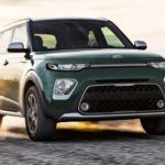 A green kia soul is driving on the road.