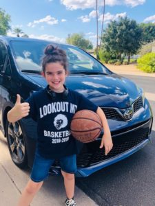 A girl holding a basketball in front of a car.