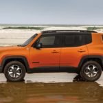 A jeep renegade parked on the beach near water.