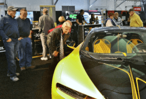 A man looking at a yellow car in a showroom.