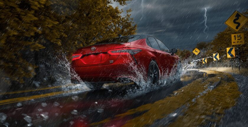 A red car driving through water on the road.
