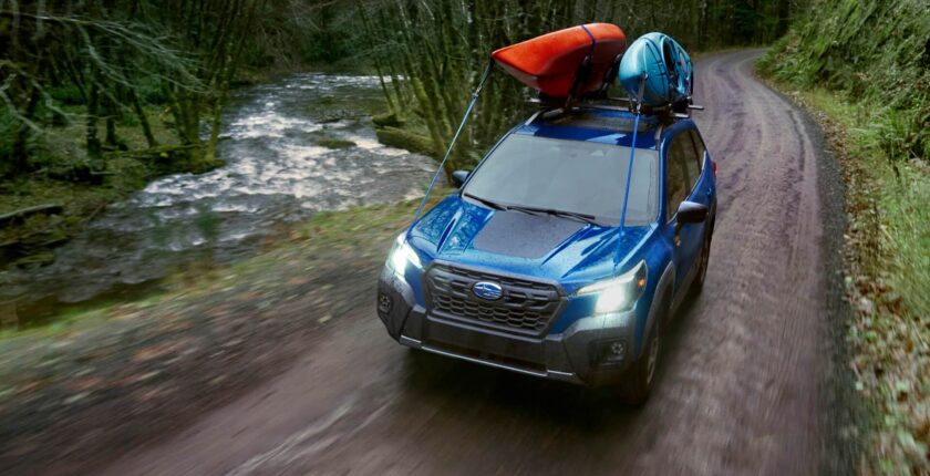 A blue suv driving down the road with a canoe on top of it.