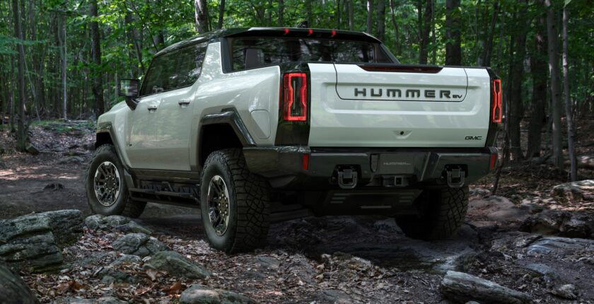A white hummer truck is parked in the woods.