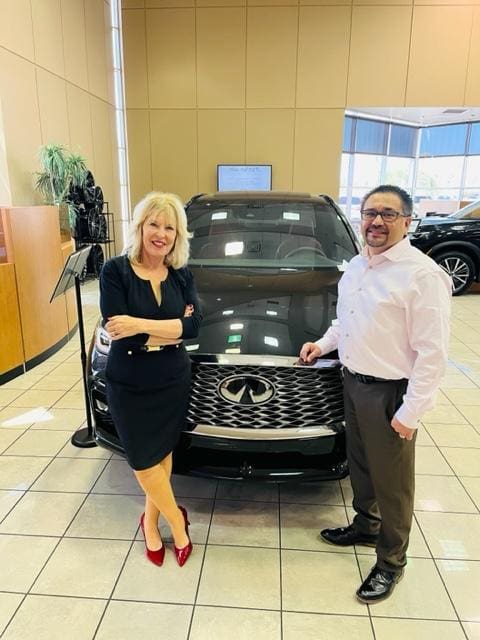 A man and woman standing in front of an infiniti car.