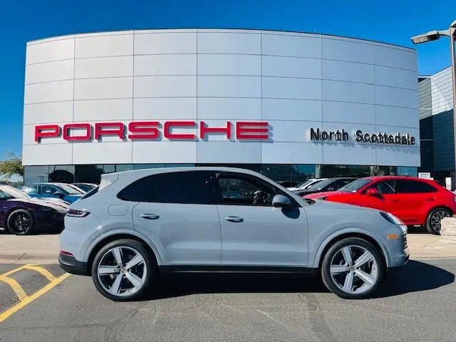 A white car parked in front of a porsche dealership.